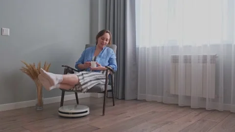 The robot vacuum cleaner cleans the room, and the girl is resting Vidéo 170903898
