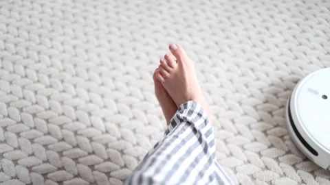 Robot vacuum cleaner driving around barefoot woman at home. Stock Footage 328034785
