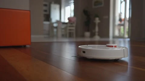 A robot vacuum cleaner efficiently navigates and cleans the parquet floor. Stock Footage 334729522