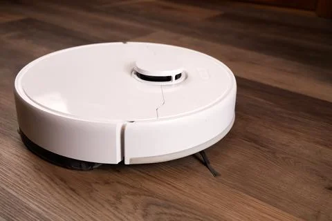 A robot vacuum cleaner moves across the wooden floor in the living room Stock-Fotos
