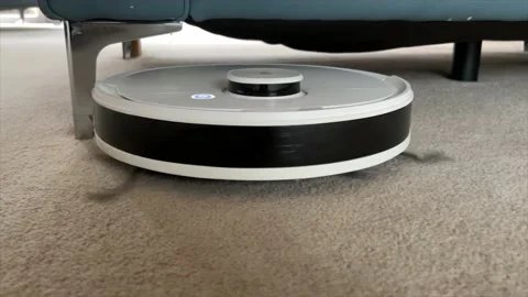 Robot Vacuum cleaner moving around a beige carpet under furniture Stock Footage 232514507