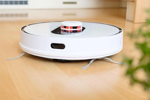 Robot vacuum cleaner performs cleaning of the room on the wooden floor. Stock Photos