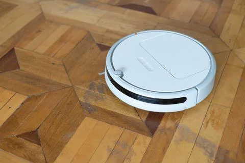 Robot vacuum cleaner stands on the light parquet floor, top view. Stock Photos