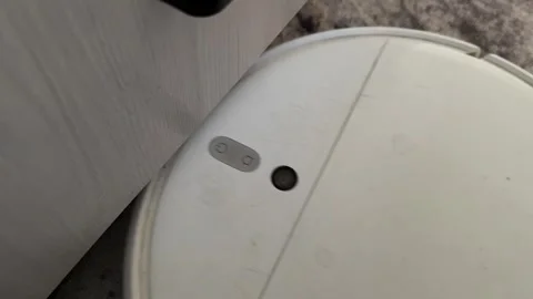 Robot vacuum cleaner trying to pass under cabinet and bumping into furniture Stock Footage 337120887