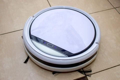 Robot vacuum cleaner working in the kitchen, sweeping debris from the tile floor Foto stock