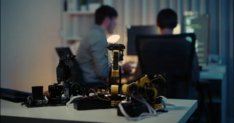 Robotic Arm Prototypes on Desk with Programmers Coding in Background. Stock Footage 306739591