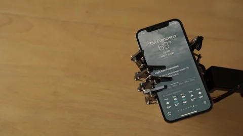 Robotic Hand Holding a Mobile with San Francisco Weather on the Screen Stock Footage 255167151
