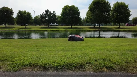 Robotic lawnmower mowing a lawn next to a scenic pond in Westerville, Ohio Stock Footage 341707372