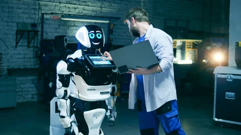 Robotic research engineer with a laptop is observing a robot-like machine Video stock 146960176