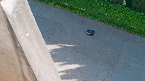 Robotic vacuum cleaner moving along sunlit outdoor concrete path Видео 337401737
