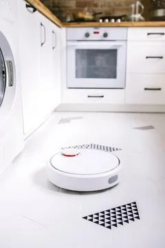 Robotic vacuum cleaner working in the kitchen. Stock Photos