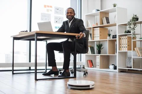 Robotic vacuum cleaning office while man working on laptop Stock Photos