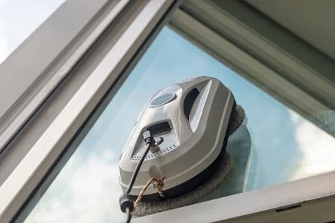 Robotic window cleaner smoothly glides on exterior glass, reflecting blue sky Stock Photos