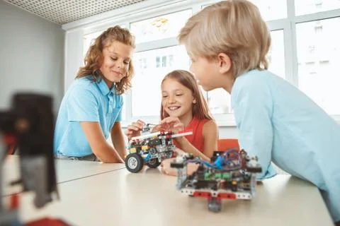 Robotics. Children having class sitting making robots connecting wires smiling Foto stock