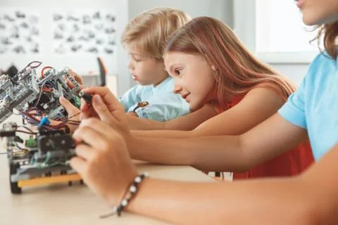Robotics. Children having class sitting making robots smiling concentrated side Stock Photos