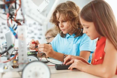 Robotics. Children sitting having class making robots girl helping friend Stock Photos