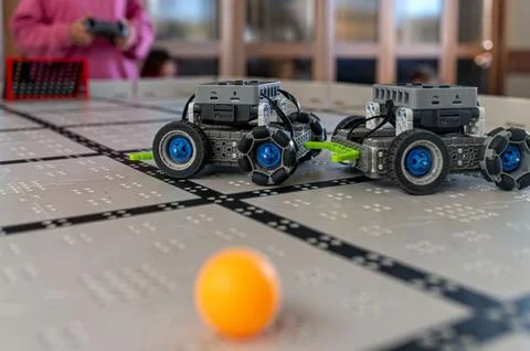 Robots interact with a ball on a grid surface during a technology demonstrati Stock Photos