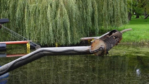 A robust metal object with textured parts dips into the calm, algae-covered.. Stock Footage 321918267