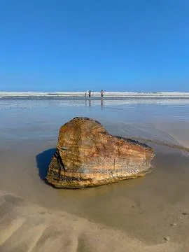 Rock on the beach with distant figures Stock Photos