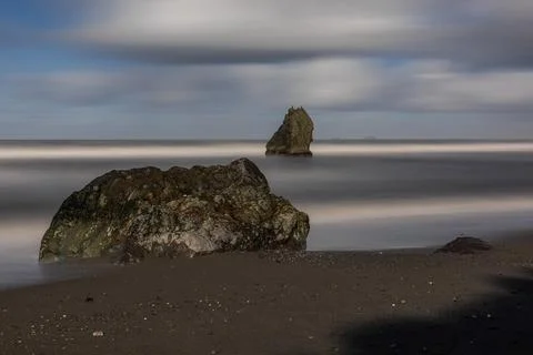 A rock is on the beach next to the water Stock Photos