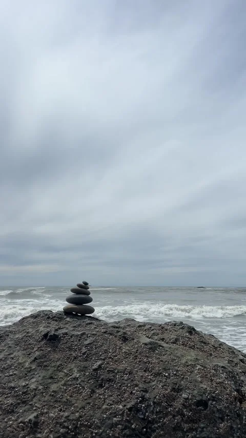A rock cairn sits on a large boulder at Ruby Beach with ocean waves Stock Footage 321504979