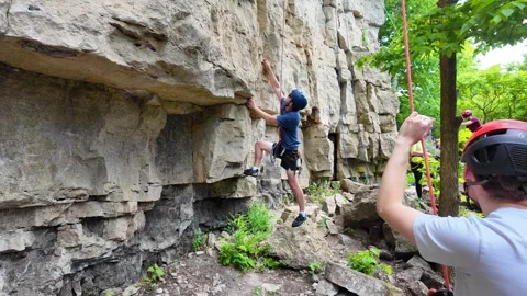 Rock climber ascending a cliff face while belayer secures the rope at the Stock Footage 343029672