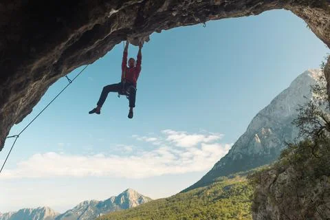 Rock climber climbs a difficult route on a rock in the form of an arch, a str Stock Photos