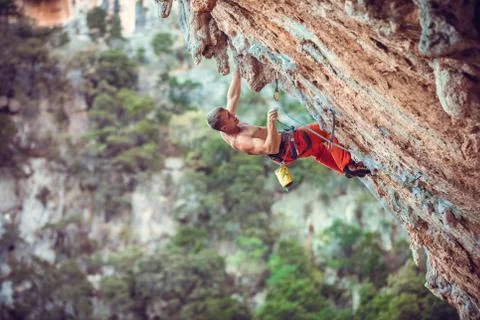 Rock climber clipping rope while climbing challenging route on cliff Stock Photos