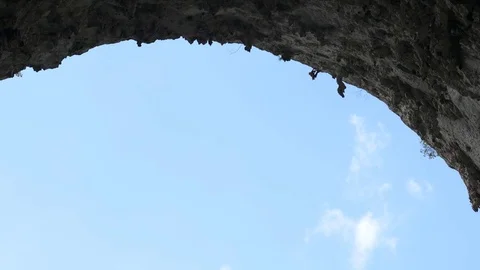 Rock climber in a Great Arch crag cave silhouetted against a blue summer sky Stock Footage 71390786
