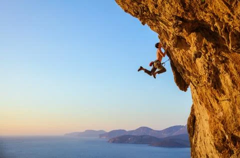Rock climber jumping on handholds while climbing overhanging cliff Stock Photos