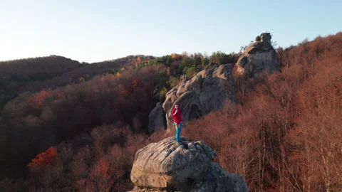 Rock climber pauses on top of boulder in evening light, overlooking colorful Stock Footage 346709339
