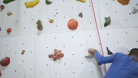 Rock climber practicing on a bouldering climbing wall, inside with colored hooks Stock Footage 123213563