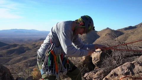 A rock climber setting up a rappel anchor on a mountain summit Stock Footage 304434496