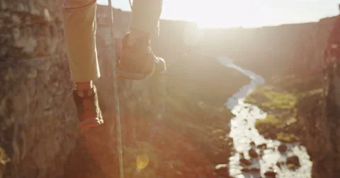 Rock climbers ascending ropes in front of sun flare above a canyon Stock Footage 64352869