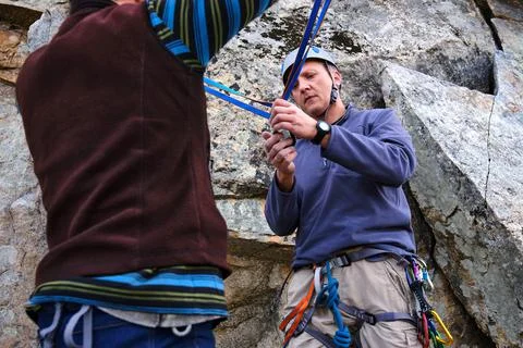 Rock climbing instructor is teaching how to perform the belay station. Stock Photos