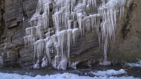 Rock covered with icicles and ice near a mountain stream near a glacier Stock Footage 123560463