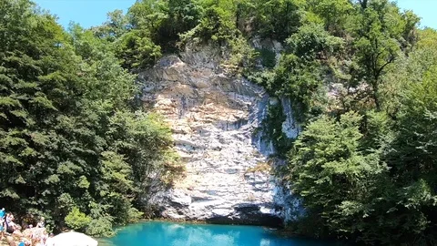 Rock covered with trees below a blue mountain lake wide lens Stock Footage 104535747