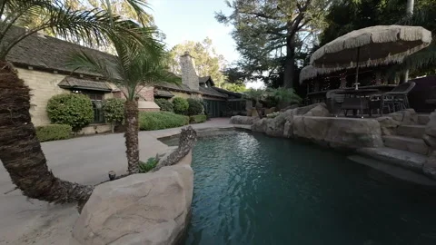 Rock-edged backyard pool beside a cottage with a brick chimney Stock Footage 345544074