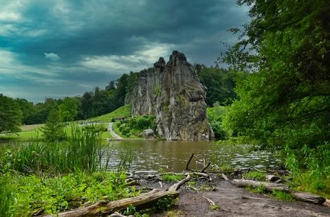 Rock formation by water under cloudy sky in a park with greenery around Stock Photos