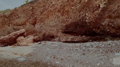 A rock hangs over the seashore. Pebble beach under the cliff. Greece. Stock Footage 288107567