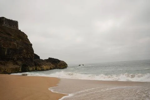 Rock next to a sandy beach on a cloudy day Stock Photos