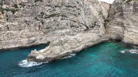 Rock stack rises from turquoise gorge limestone cliffs xaqqa cliffs malta aerial Stock Footage 343577308