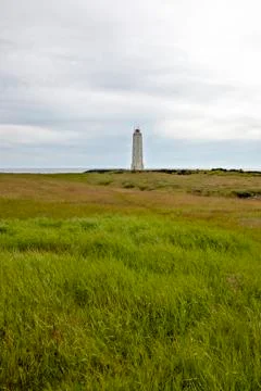 Rocket-shaped lighthouse at the end of a large green meadow with the sea in t Stock Photos