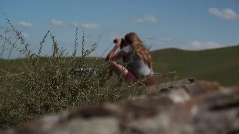 Rocks and grass, behind which a blurred girl sits and looks through binoculars. Stock Footage 258359974
