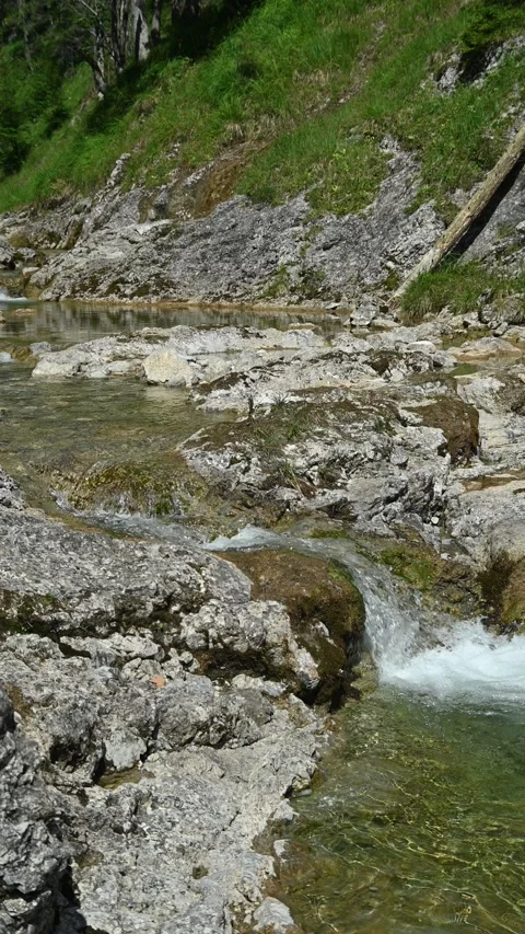 Rocks and a small waterfall from a mountain stream in summer sunlight, vertical  Video stock 260876157