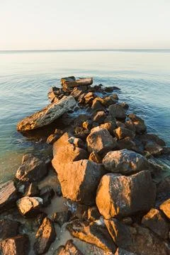 Rocks arranged in a line extend into still water at sunset, showing a natural Stock Photos