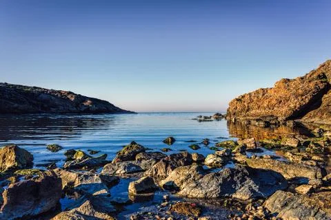 Rocks next to a pebble beach under blue skies Stock Photos