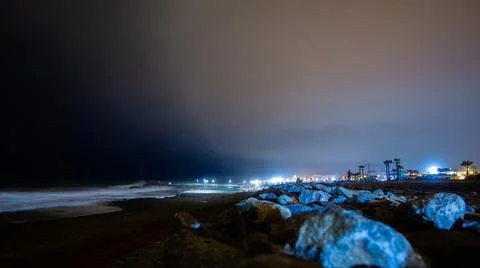 Rocks, pool lights in a cloudy night above the sea Stock Photos