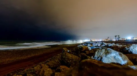 Rocks, pool lights in a cloudy night above the sea Stock Photos