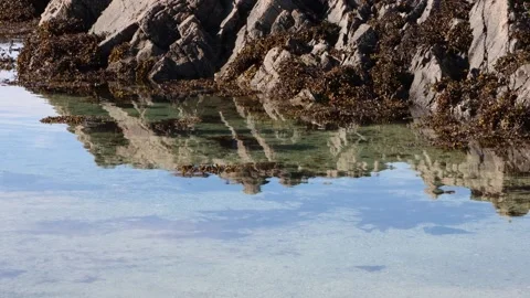 Rocks reflected in shiny flat sea water on sunny day Stock Footage 335540148